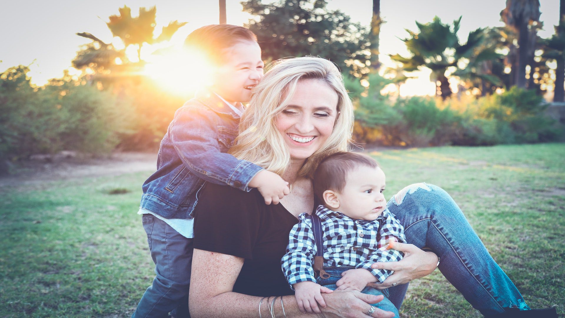 A mom holding her two children in her arms at sunset.