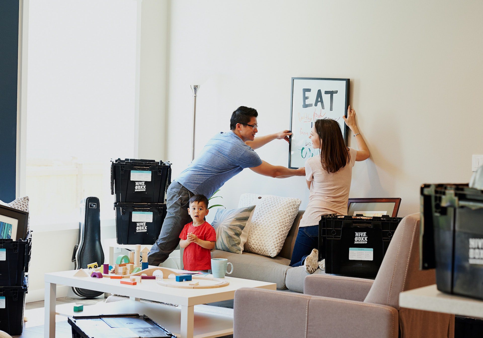 A husband and wife move into their new house while their child stands and watches.