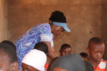 A woman stands in a classroom helping children.