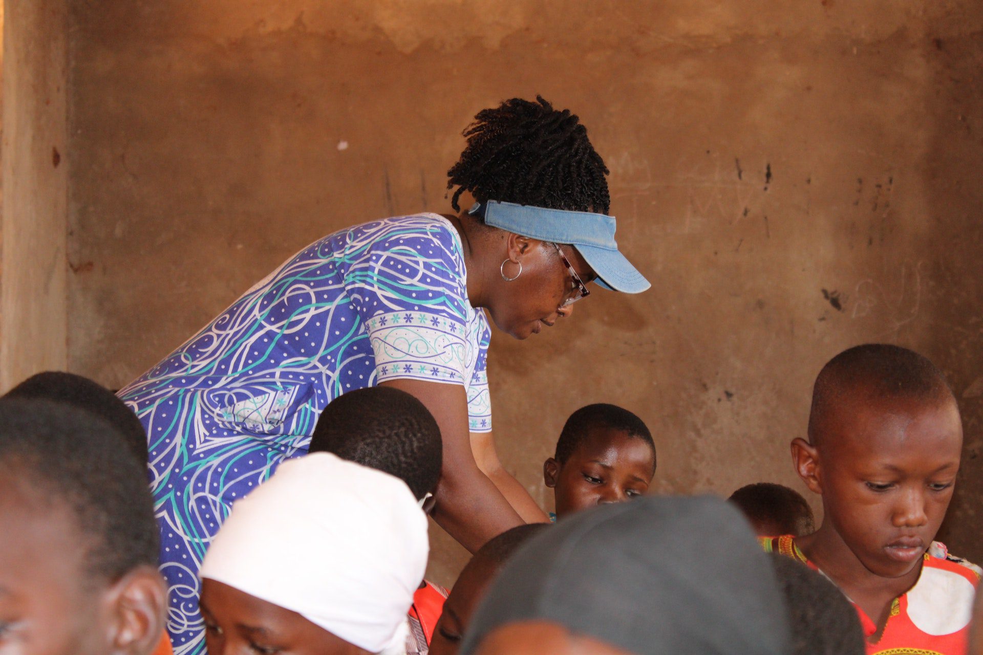 A woman stands in a classroom helping children.