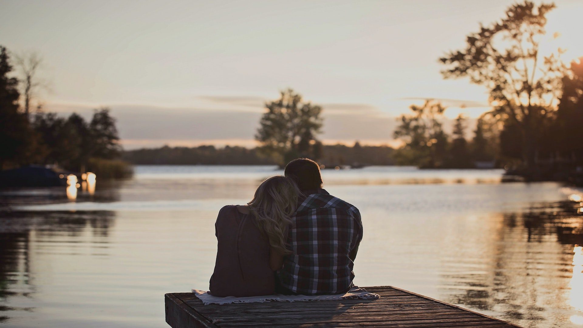 Man and woman sitting on a dock during a sunset.