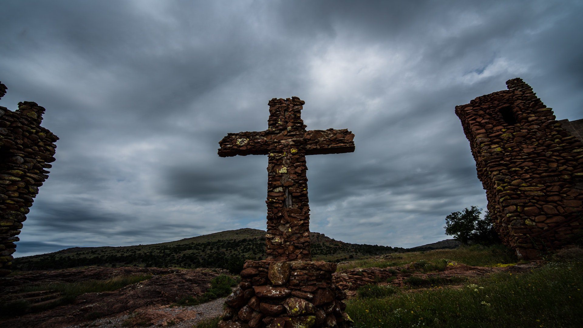 Brown stone cross in a green field under a gray sky.