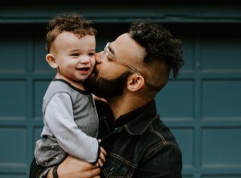 A man with glasses holds his child and kisses him on the cheek.