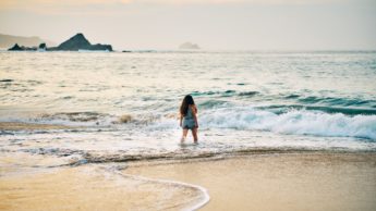 Woman standing in ocean water near sand.
