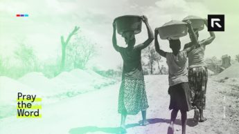 Three women walk with baskets on their heads.