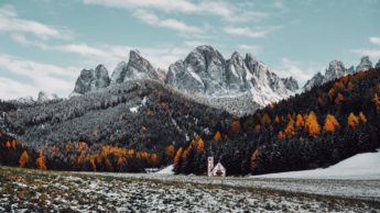 White church in snowy field near mountains.