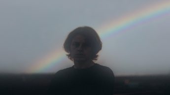 Man in a black shirt standing in front of a rainbow.
