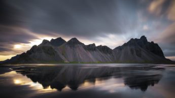 Gray mountains under a cloudy sky near water.