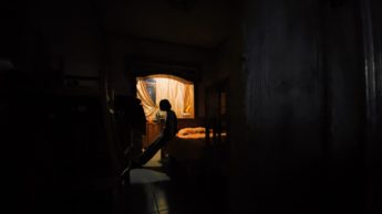 Silhouette of a woman sitting on a bed in front of a window.