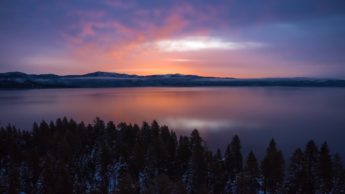 Sunrise over lake and tree covered mountains.