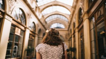 Back of a woman walking in a brown building with a glass roof.
