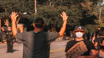 Man with his arms raised and another man holding a sign on a street.