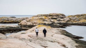 Two people walking on rocks near water.