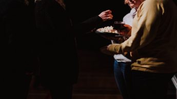 Three people standing with a plate of bread and a glass of wine.