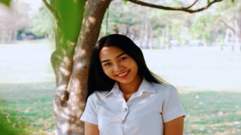 Smiling woman in a white shirt standing in front of a tree.