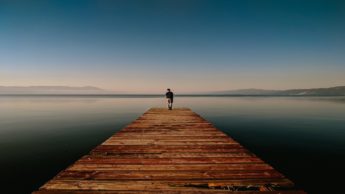 Man standing at the end of a wooden dock near water.