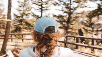 Back of a woman in a blue hat in front of trees.
