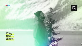 A man with a jacket stands next to a snowy lake.