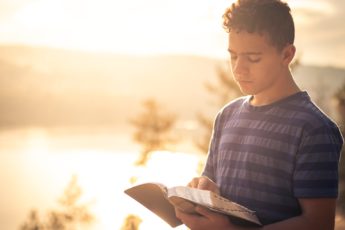 A man stands and reads his Bible next to the lake.