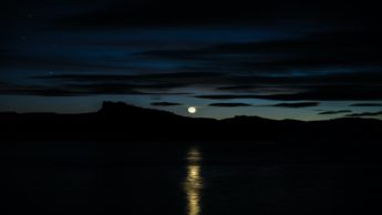 Moon in a night sky over water.