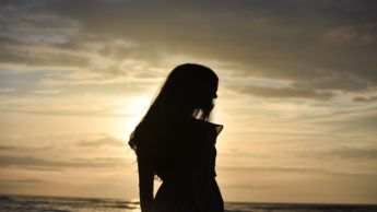 Silhouette of a woman facing right in front of an ocean.