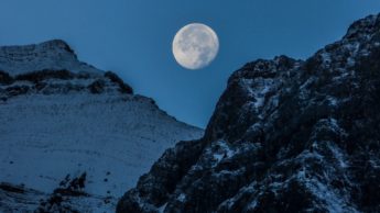 Moon over snowy, rocky mountains.