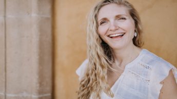 Woman in a white shirt smiling in front of a yellow wall.