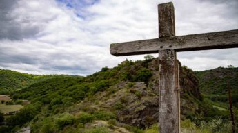 Wooden cross on a green hill.