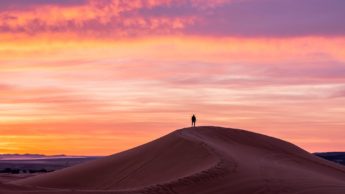 Silhouette of a man standing on a sand dune during a sunset.