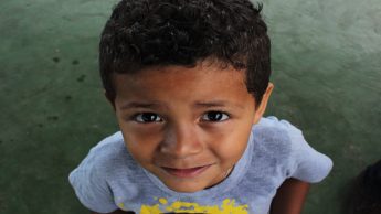 Young boy in a gray shirt standing on a green floor.