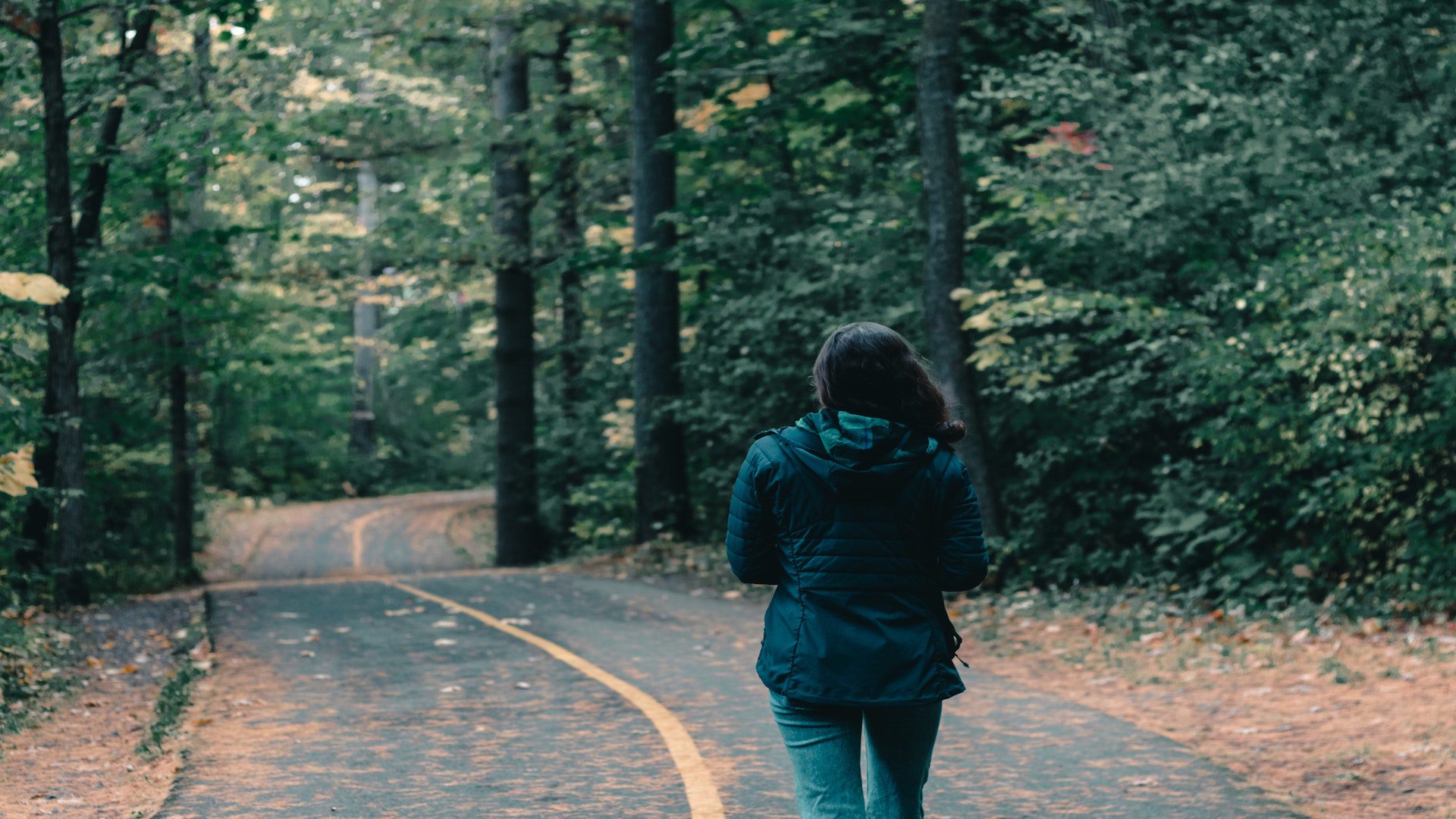 Woman walking on a road surrounded by trees.