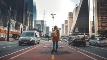Woman wearing a backpack walking in the middle of a city street.