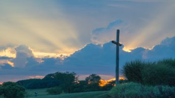 Cross on green grass under a cloudy sky.