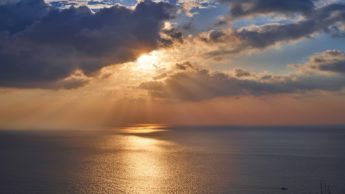 Sun streaming through clouds over ocean.