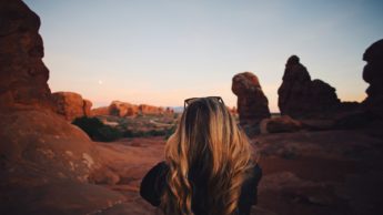 Back of a woman standing in front of red rocks.