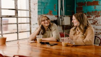 Two women sitting at a table with cups of coffee.