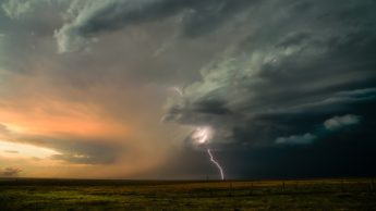 Lightning and dark clouds over a green field.