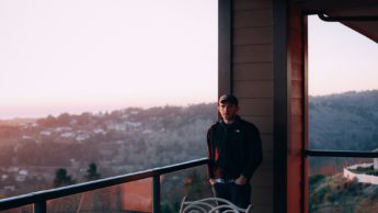 Man standing on porch near hill.
