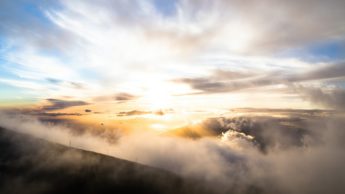 Sun streaming through clouds above mountains.
