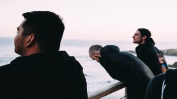 Three men leaning against a railing over an ocean.