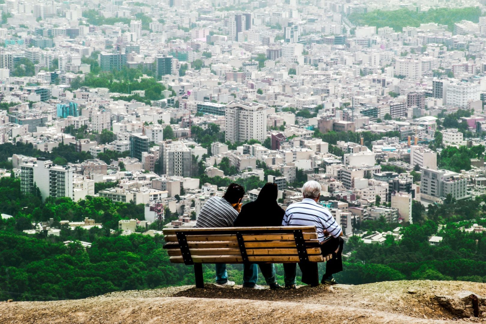 Three people and sit overlooking a city in Iran.