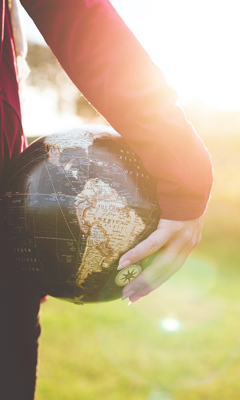 person holding world globe while staring to the horizon