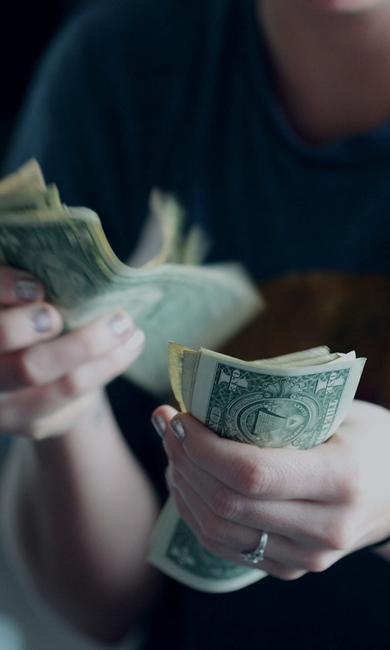 A young woman counting dollar bills.