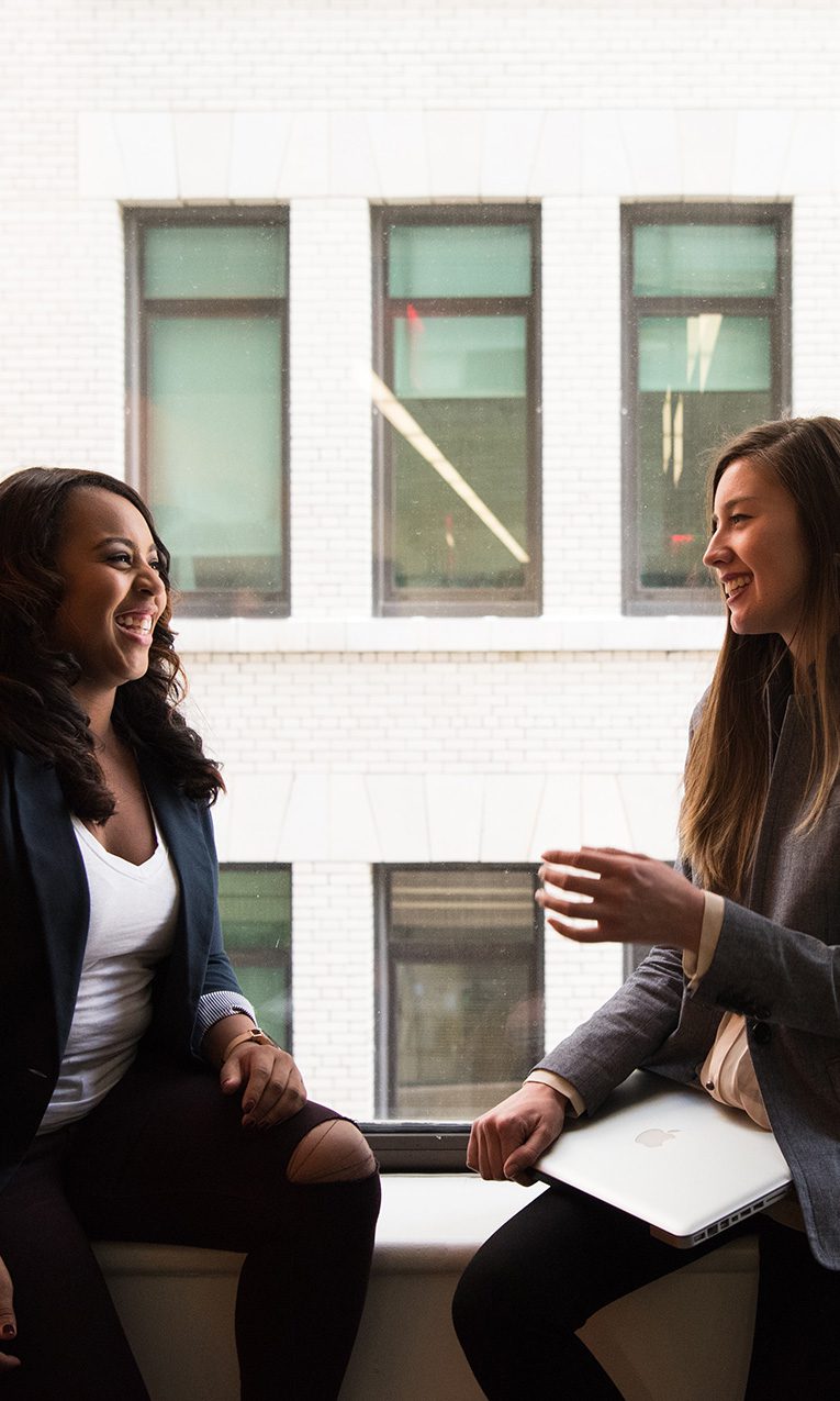 two women talking sitting by a large window
