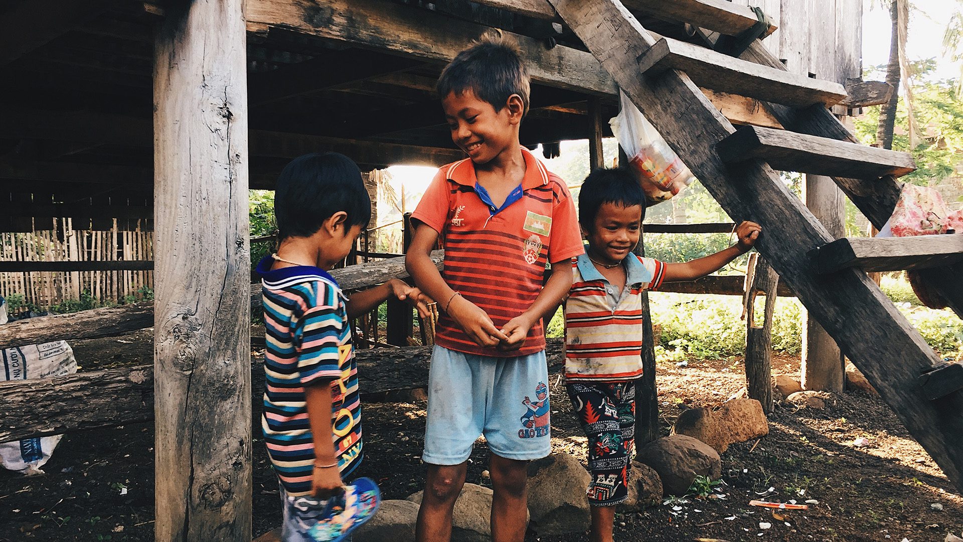3 boys standing by brown wooden house