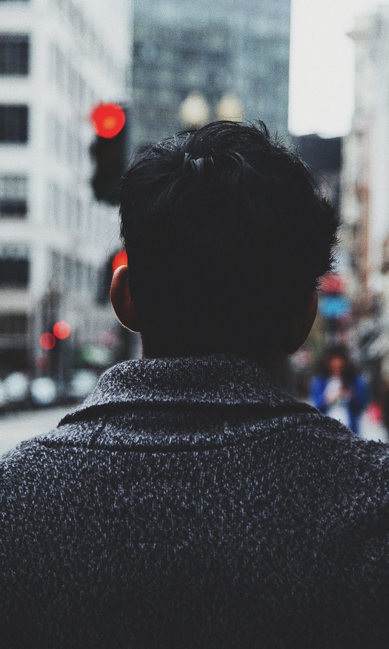 man on road along concrete buildings during daytime