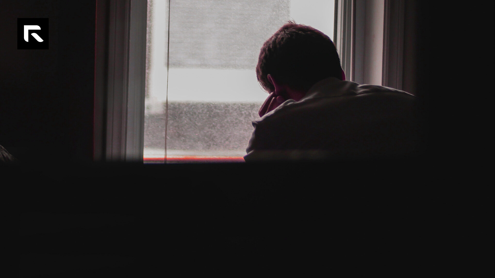 a man sitting hunched over and looking out a window
