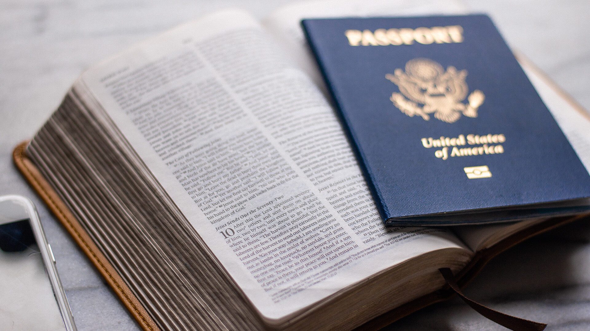 A passport sits on an open Bible beside a phone