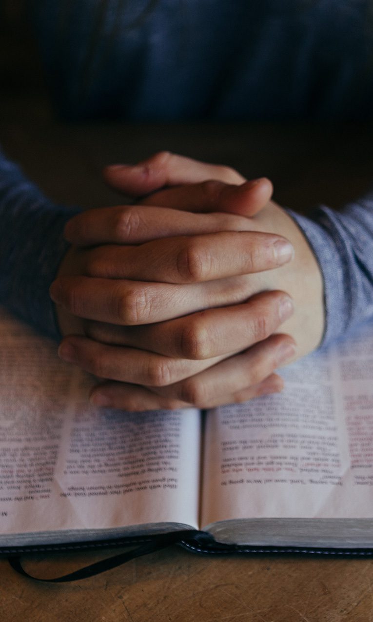 man with hands folded over the Bible in prayer