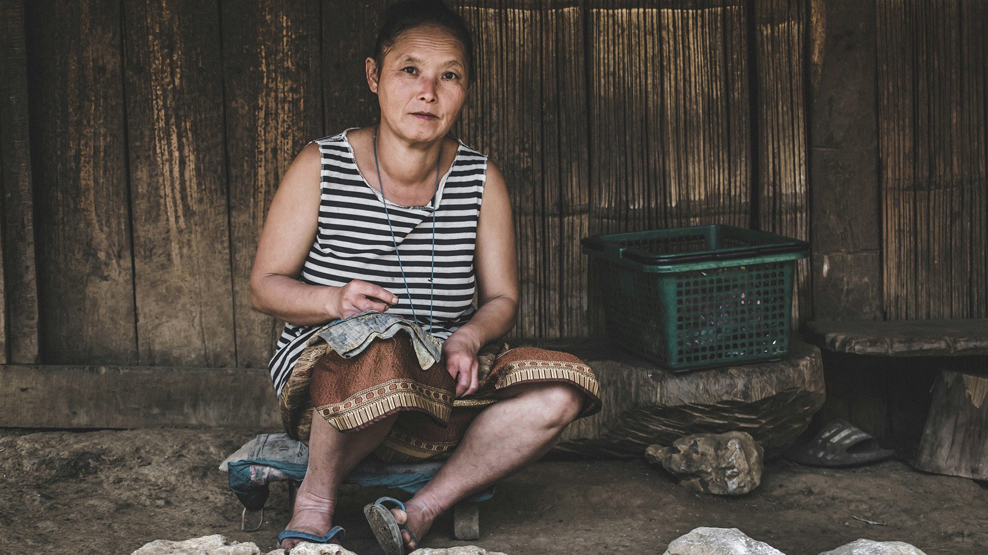 Hmong woman sitting near green plastic basket outside